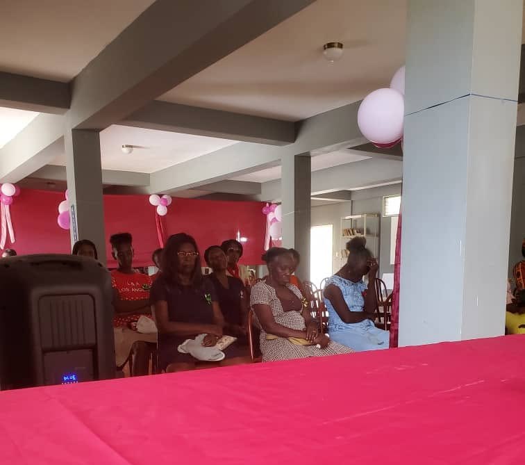 Women of the commune seated in a hall decorated in pink for a Mother’s Day celebration