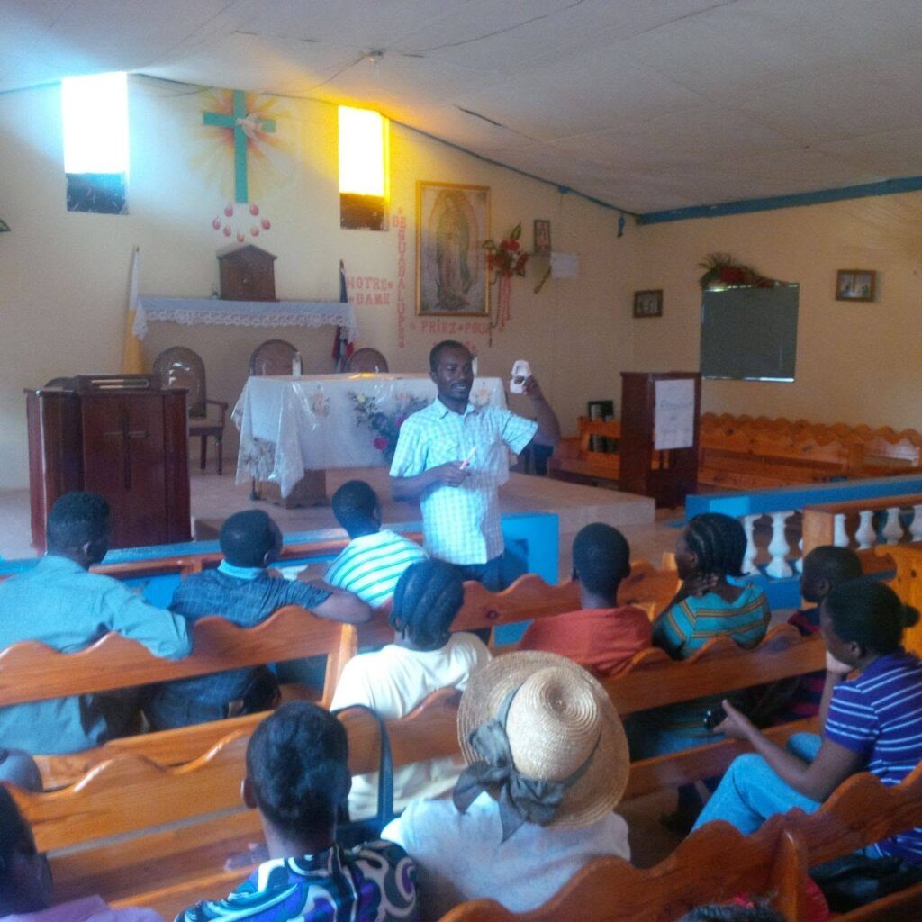 A trainer demonstrating dental hygiene to an audience seated in the pews of the Catholic church